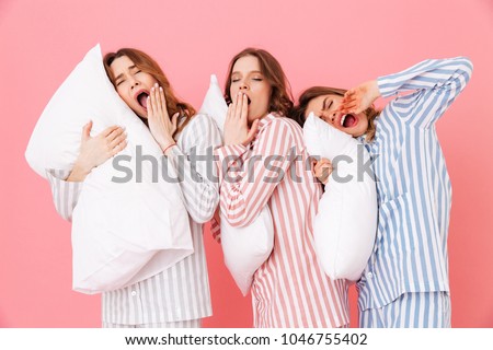 Portrait of sleeping women 20s in homewear having fun while resting at home together and yawning due to insomnia isolated over pink background Royalty-Free Stock Photo #1046755402
