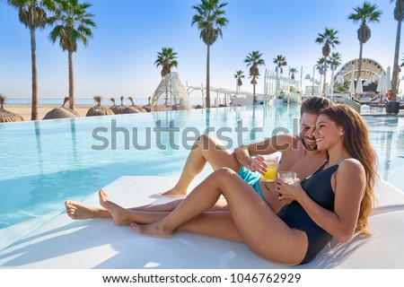 Young tourist couple on infinity pool hammock at resort on the beach drinking soda