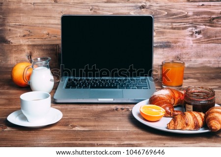 Laptop, cup of coffee, milk and croissants, orange, bun, handmade jam,  for a business breakfast on the wooden background in morning