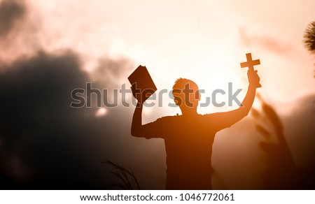 Young man hands holding holy Bible and lift of christian cross with light sunset background. christian concept