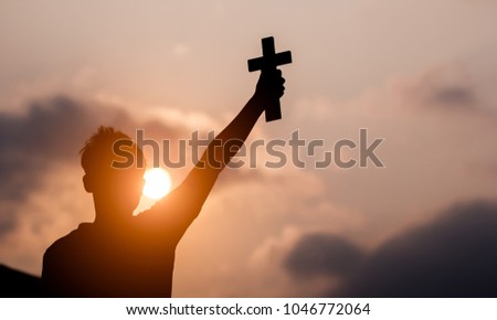 Young man hand holding and lift of christian cross with light sunset background