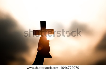 Young man hand holding and lift of christian cross with light sunset background