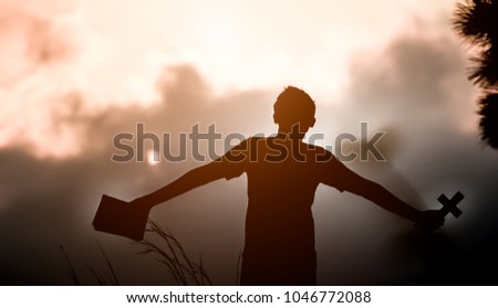 Young man holding Holy Bible and christian cross with light sunset background
