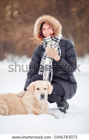 Photo of happy woman in scarf sitting next to labrador at winter