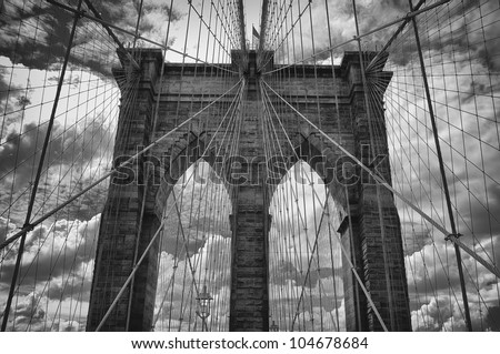 Dramatic black and white view of the historic Brooklyn Bridge with ominous clouds in the background.