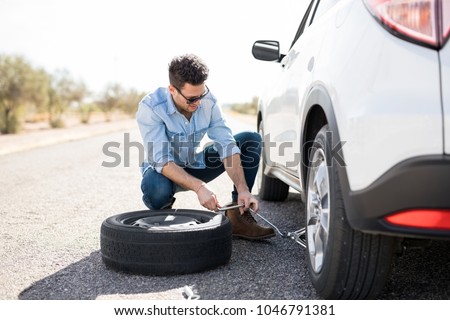 Handsome young man lifting the car on the jack for changing flat tire on the road Royalty-Free Stock Photo #1046791381