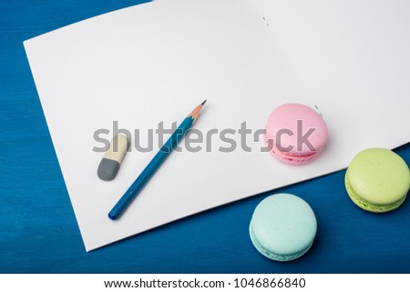 Template clean notebook with pencil and eraser on a blue background. Color makarons cookies. Copy space 