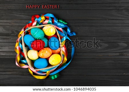 Text Happy easter! Greeting card with Easter colored eggs on a black background, colorful ribbons, basket, copy spase