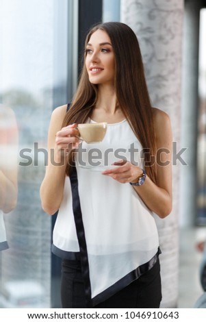 Young brunette drinking capuchino in the restorant near the window. Stylish lady drinking capuchino