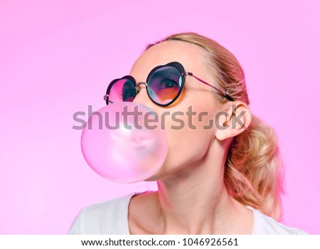 girl with chewing gum on a pink background with glasses Royalty-Free Stock Photo #1046926561