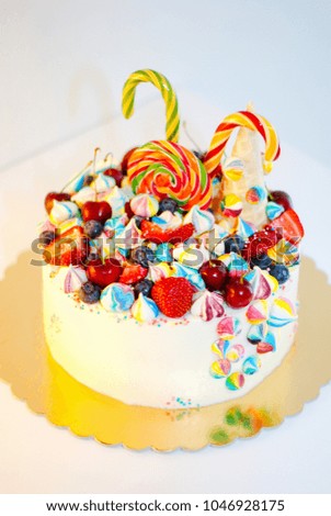 A beautiful white cake decorated with strawberries, blueberries and sugar candies on top. The concept of the desserts for the birthday