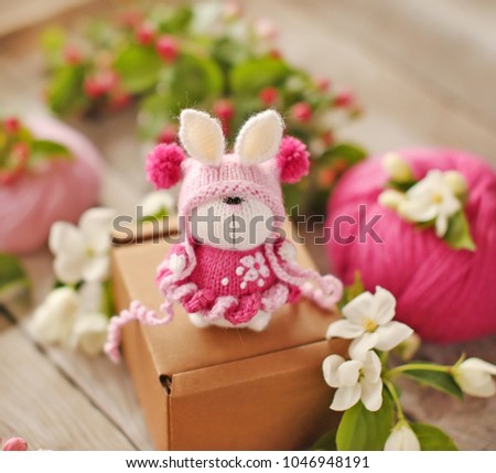 Handmade  knitted toy. Easter bunny in a pink dress among apple flowers . 