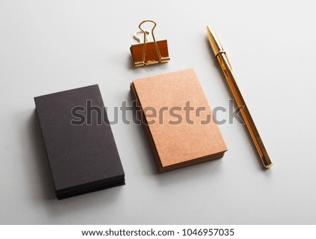 Top view of business cards of brown and black color next to clip and golden ball pen on gray background. Mockup.