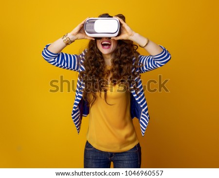 happy modern woman with long wavy brunette hair against yellow background using VR gear