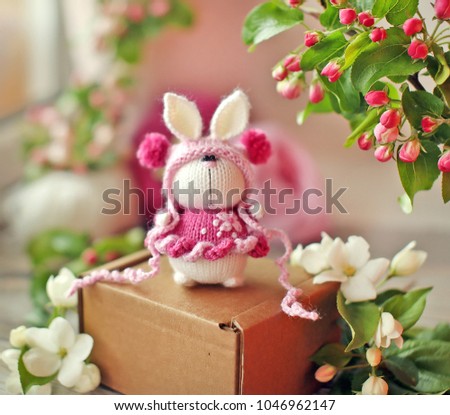 Handmade knitted toy. Easter Bunny in a pink dress on spring background with apple flowers 