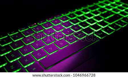 Gamer keyboard with green backlight, modern laptop computer.