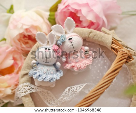 Handmade knitted toys. Easter bunnies in pink and blue dresses in basket with balls of yarn on a floral background with peonies