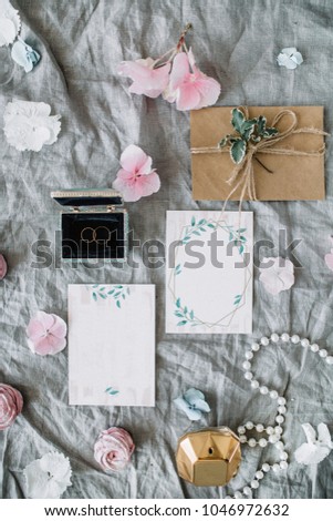 Wedding invitation cards, envelopes, rings, decoration and pink flower buds on grey blanket. Bridal flat lay, top view concept