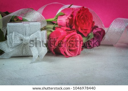 Celebratory background of roses and a silvery gift box with ribbon, close-up with place for text
