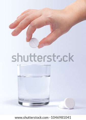 A female hand holding a round effervescent pill over a glass of water on a light background