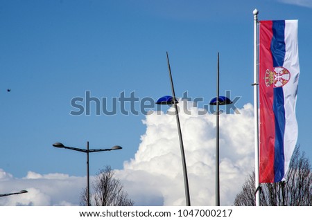 Street lighting in the background incredible large white clouds also the picture shows the flag of the republic of Serbia.