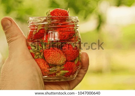 Glass jar with red strawberry in hand