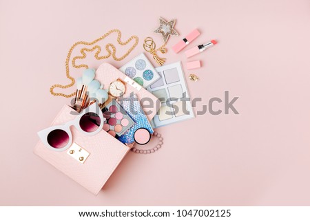 Cosmetic products flowing from Makeup bag on pastel pink background.  Flat lay, top view. Fashion concept Royalty-Free Stock Photo #1047002125
