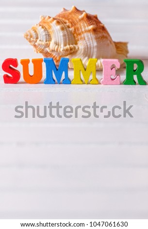 Sea shell with colorful 'SUMMER TRAVEL' phrase on white wooden table top
