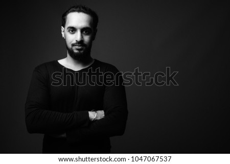 Studio shot of young bearded Indian man against black background in black and white