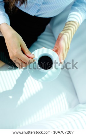 Photo of porcelain cup with strong black coffee and saucer in female hands
