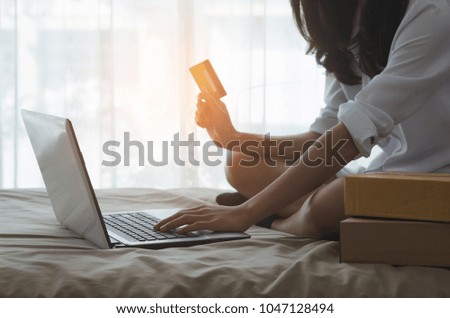 attractive business woman holding credit card and using laptop with typing on keyboard for searching shopping online on the bed in bedroom.