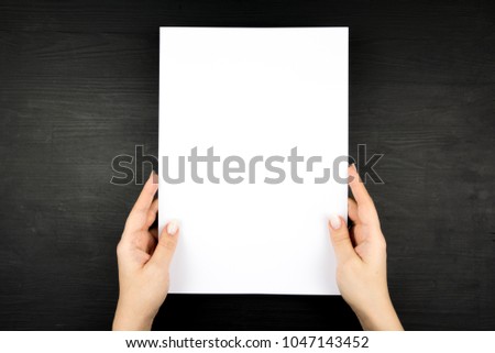 Woman holding blank sheet of paper on black wooden background. Mock up for design. Royalty-Free Stock Photo #1047143452