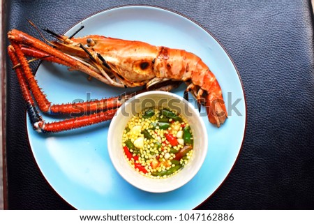 Delicious big river grilled shrimp on blue dish with bowl of chili sauce in Thai style on black background, Tasty seafood for summer barbecue party concept, top view picture