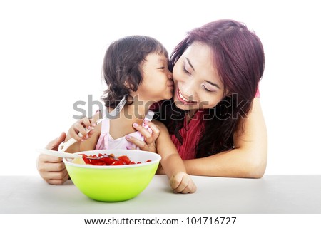 Cute asian little girl with fruit salad kissing her mother