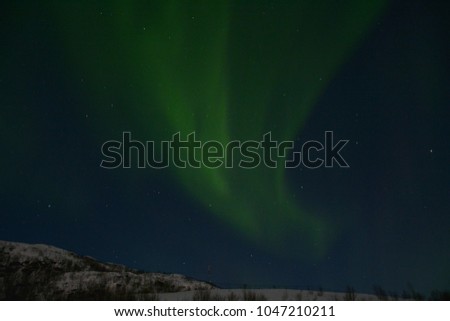 TROMSO, NORWAY - MARCH 6, 2017: The northern lights (Aurora Borealis) over Seljelvnes, Troms by the sea and the snowy mountains