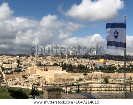 Israeli flag with a Star of David flying over Jerusalem; with Dome of the Rock and the Temple Mount, the rooftops of the Old City and the new city of West Jerusalem skyline in the background
