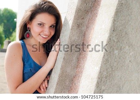 Portrait of a beautiful young woman happy smiling standing and posing outdoors in the spring or summer reclining on the concrete structure