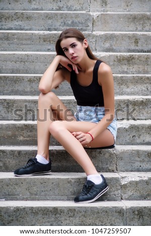 Young beautiful girl sitting on the stairs looking at camera. Vertical photo