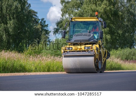 Yellow heavy vibration roller at asphalt pavement works. Road repairing in city. Road construction workers repairing highway road on sunny summer day. Heavy machinery, loaders and trucks. 