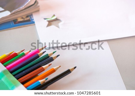 Creative workshop for kids. Pile of sharp coloured drawing pencils on table. Cutting out stars and making decorations from white paper. Concept of art, crafts and kids having fun 