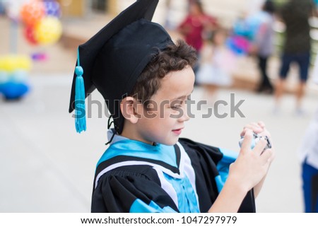 a  boy graduated at kindergarten school  holding his camera to take a picture