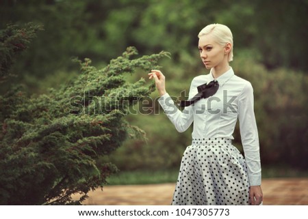 Blonde in a retro style skirt and blouse next to a tree. The girl goes to the garden in a vintage dress.