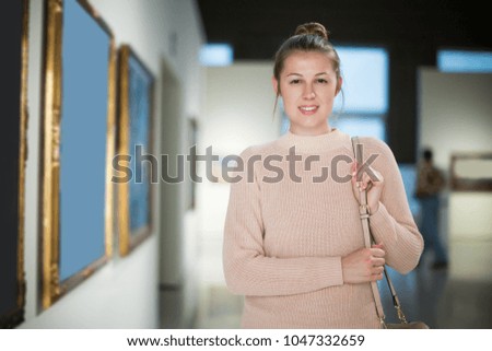 Positive adult woman visitor in the art museum looking at picture collection