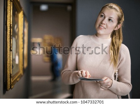 Portrait of young woman with guide looking at pictures in a museum of arts 
