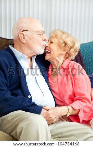 Senior couple relaxing at home, she's laughing as he kisses her nose.
