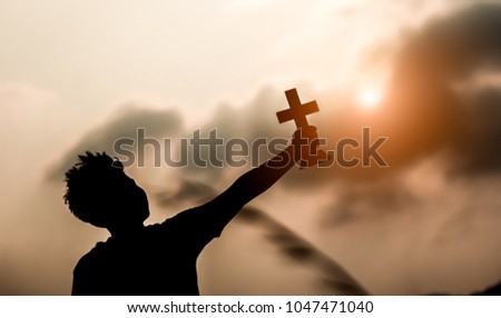 Young man holding cross and look up to the sky with light of suny