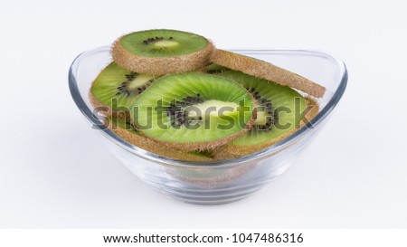 Green slices of kiwi in oval glass bowl. Fuzzy kiwifruit. Actinidia deliciosa. Beautiful close-up of the heap of sliced tropical fruits with brown skin on a white background.