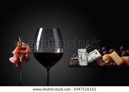 Glass of red wine with various cheeses , grapes and prosciutto on a black background.