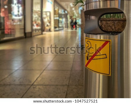 Garbage is at a shopping center with a sign on it that prohibits smoking. Concept: cleanliness