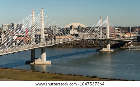 It's a clear day in Portland Oregon at Tilikum Crossing as people traverse the river with Mount St. Helens in the background
